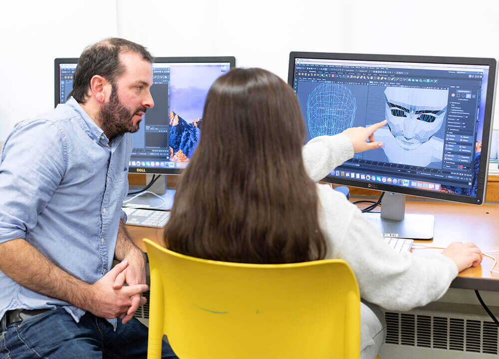 A game design and development student works on the 3D-modeling of one of her characters with the help of a professor